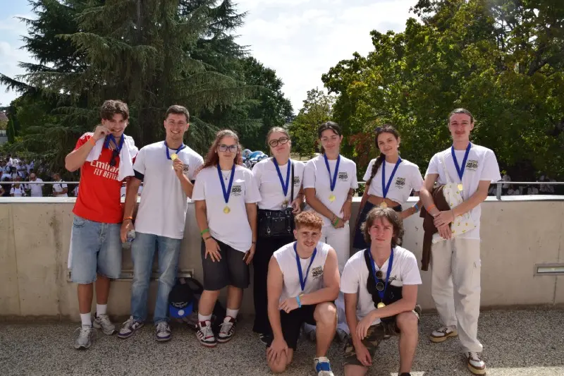 Groupe de jeunes étudiants vainqueurs portant des t-shirts blancs et des médailles autour du cou devant le parc.