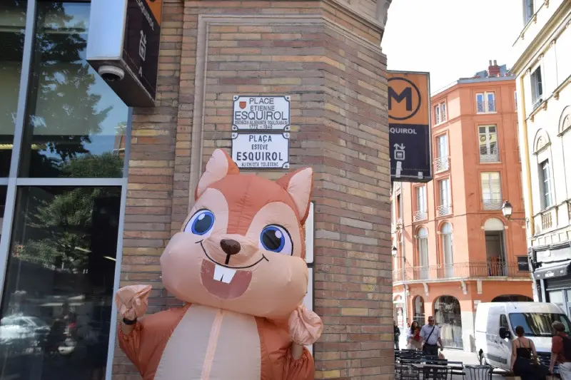 Mascotte écureuil gonflable posant sous la plaque de la place Esquirol lors de la Journée d'Intégration à Toulouse organisée par l'Institut Limayrac.